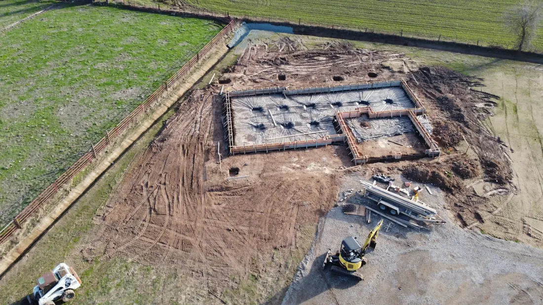 Aerial view of a fresh concrete foundation on a cleared lot with an excavator