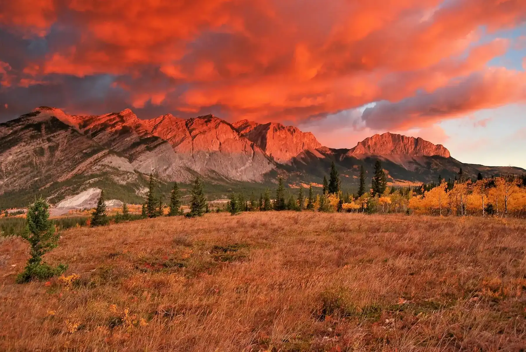 Mountains and autumn grassland under a fiery red sunset sky