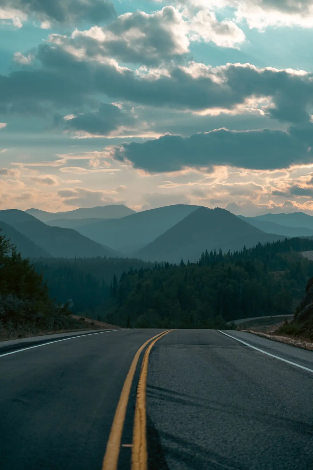 Two-lane highway leading into forested mountains under a cloudy sky