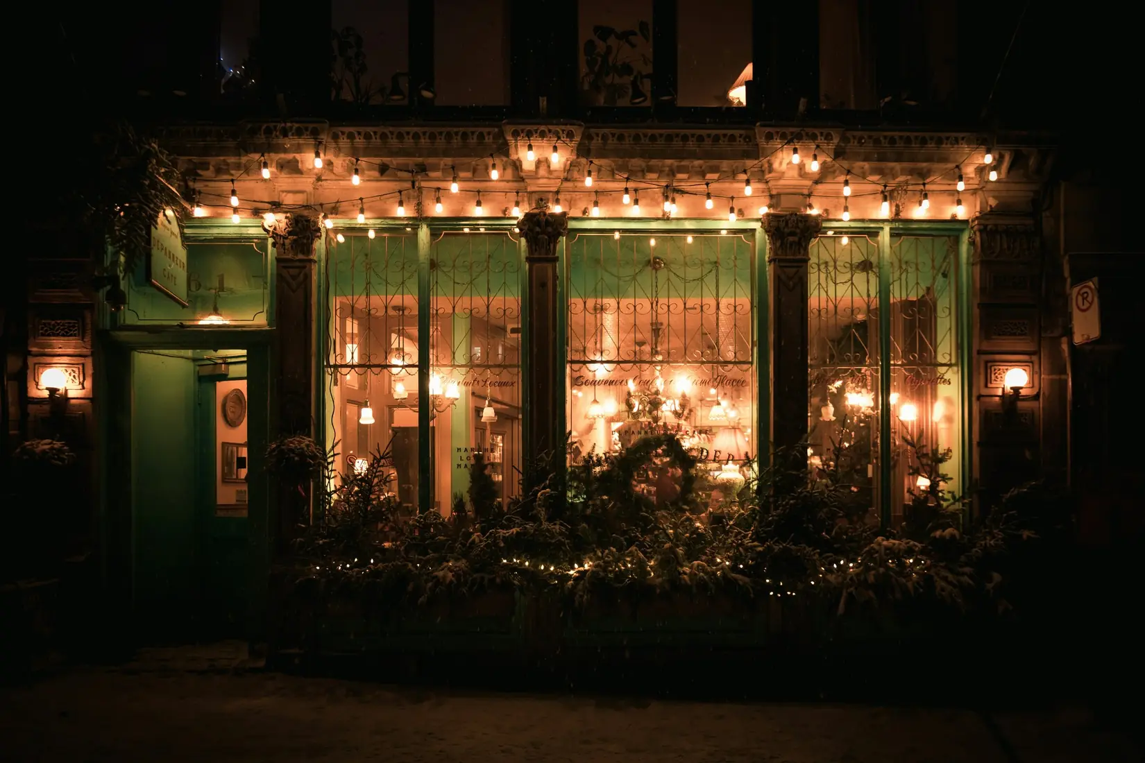 Storefront glowing with string lights and greenery at night